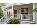 Close up of covered front porch with white railings, a red door with wreath, seating, and lush landscaping at 3923 Napa Valley Dr, Raleigh, NC 27612