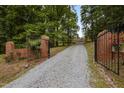 Gated gravel driveway leading to secluded home surrounded by lush trees at 12088 Burlington Rd, Hurdle Mills, NC 27541