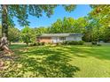 Charming single-story home with a spacious front yard and mature trees under a bright blue sky at 1593 E Washington Ave, Creedmoor, NC 27522