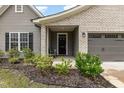 Inviting front entrance featuring a covered porch, brick accents, manicured shrubs, and a well-maintained lawn at 1828 Wellspring Ct, Graham, NC 27253