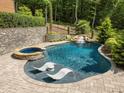 Beautiful pool area with lounge chairs in the water, a waterfall, and hot tub, surrounded by stone pavers at 4312 Mystic Ln, Hillsborough, NC 27278