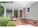 Cozy front porch featuring brick steps, white railings, a red door, and a comfortable seating area with plants at 108 Ripplewater Ln, Cary, NC 27518