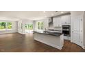 Open-concept kitchen featuring a large island, white cabinets, stainless steel appliances, and wood flooring at 2332 Horton Park Dr, Apex, NC 27539