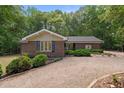 Inviting brick ranch home featuring lush landscaping and a spacious gravel driveway, nestled among mature trees at 1134 Deerfoot Trail Trl, Sanford, NC 27332