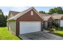 Side angle of a brick home featuring a white two car garage, dark shutters, and manicured landscaping at 3027 Maple Ave # U1, Burlington, NC 27215