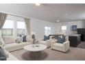 Bright living room featuring large windows, neutral-toned furniture, and an open concept layout to kitchen and dining area at 153 Gladstone Loop, Clayton, NC 27520
