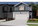 New two-story townhome exterior, featuring an attached garage, concrete driveway, manicured lawn, and colorful flowerbeds at 1027 Winding Spring Dr, Mebane, NC 27302