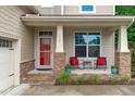 Inviting covered porch with stylish chairs, a red door, and stone accents at 1939 Mostyn Ln, Apex, NC 27502