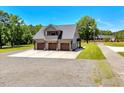 Aerial view of a three-car garage with an upper balcony, surrounded by lush greenery and a spacious driveway at 2258 Sanders Rd, Stem, NC 27581