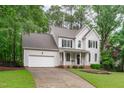 Traditional two-story home with attached garage, front porch, and manicured lawn surrounded by mature trees at 1208 Mossy Glade Cir, Apex, NC 27502