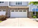View of the front of a two car garage with stone accents and a concrete driveway, surrounded by landscaping and partial house view at 1021 Benay Rd, Morrisville, NC 27560
