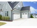 View of home's three-car garage featuring bright white doors, gray siding, and clean concrete driveway at 7736 Roberts Rd, Apex, NC 27523
