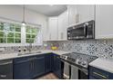 Modern kitchen featuring blue lower cabinets, white upper cabinets, stainless steel appliances, and patterned backsplash at 103 Lake Tillery Dr, Cary, NC 27519