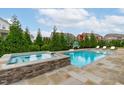 Inviting backyard pool and spa area surrounded by lush greenery and a stone patio at 120 Hazel Alder Ct, Holly Springs, NC 27540