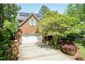 View of the side of the brick home with a two-car garage and solar panels on the roof at 126 Solterra Way, Durham, NC 27705