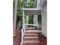 A covered porch with brick steps, white railings, and a cozy chair to enjoy the natural scenery at 516 Ryan Rd, Cary, NC 27511