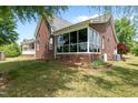 Rear exterior featuring a brick home with a sunroom filled with windows and a well-maintained lawn at 1852 Gwyn Rd, Burlington, NC 27217