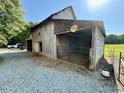 Rustic barn featuring open bay, gravel driveway, and adjacent fenced garden area at 8365 Aaron Creek Church Rd, Oxford, NC 27565