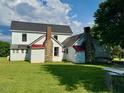 Exterior view of the white farmhouse showcasing the stone chimney and spacious backyard at 8365 Aaron Creek Church Rd, Oxford, NC 27565