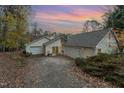View of a light colored one-story home with an attached garage and long driveway at dusk, surrounded by trees and fallen leaves at 103 Pony Express Cv, Louisburg, NC 27549