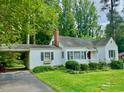 Quaint single-story home featuring a covered parking area and a red front door surrounded by green landscaping at 1609 Cypress Dr, Henderson, NC 27536