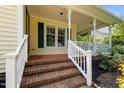 Inviting front porch with brick steps and white railings, complemented by the home's yellow siding and green shutters at 2216 Hoskins Rd, Burlington, NC 27215