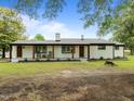 Charming white brick home boasts a covered porch with wooden columns, inviting rocking chairs, and beautifully landscaped front yard at 7042 Us 401 Highway N, Fuquay Varina, NC 27526