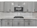 Close-up of kitchen featuring gray cabinets, stainless steel microwave and stove, and a white backsplash at 1217 Linkwood Way, Fuquay Varina, NC 27526