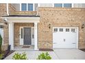 Close-up of a brick townhome featuring an attached garage, front door and manicured landscaping around the entrance at 214 George Pine Way, Knightdale, NC 27545