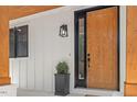 Close up of the solid wood front door with black trim, modern sconce, and landscaped entryway at 411 Bon Air Ave, Durham, NC 27704