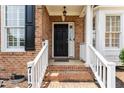 Inviting front porch with a black front door, classic white railings, and brick steps at 712 Brittley Way, Apex, NC 27502