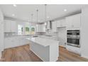 Modern, all-white kitchen boasts stainless steel appliances, quartz countertops, a central island, and stylish pendant lighting at 800 Hillfarm Dr, Wake Forest, NC 27587