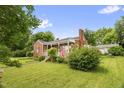 Quaint brick home with a covered front porch, an American flag, and a well-maintained lawn with mature trees at 625 Columbia Ave, Burlington, NC 27217