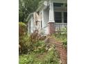 Side of a bungalow with a brick chimney and overgrown yard and plants around the foundation at 431 Charles St, Henderson, NC 27536