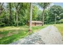 Scenic shot of a ranch-style home with gravel driveway access, surrounded by trees and greenery at 7030 Stockard Rd, Snow Camp, NC 27349