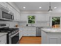 Bright kitchen featuring white cabinets, stainless steel appliances, hardwood floors, and a window view to the backyard at 1210 Eastham Dr, Apex, NC 27502
