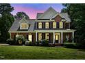 Charming two-story brick home featuring a welcoming front porch, black shutters, and manicured landscaping at dusk at 2328 Forestbluff Dr, Fuquay Varina, NC 27526