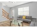 Sunlit living room featuring staircase, gray sofa, glass coffee table, and wood floors at 1002 Willow Dr # Apt 107, Chapel Hill, NC 27514