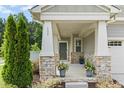 Inviting front porch featuring stone pillars, a dark front door, and decorative potted plants, adding curb appeal at 137 Azalea View Way, Holly Springs, NC 27540