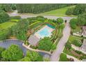 Aerial view of a community pool surrounded by lush landscaping, lounge chairs, and a nearby parking lot at 325 Wescott Ridge Dr, Holly Springs, NC 27540