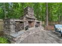 Inviting outdoor stone fireplace with wood storage, a mantel, and a patio area, perfect for relaxing in the backyard at 325 Wescott Ridge Dr, Holly Springs, NC 27540