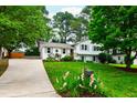Charming two-story home with white painted brick, gray shutters, mature trees, long driveway, and a lush front yard at 433 Rosehaven Dr, Raleigh, NC 27609