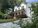 Side angle view of a two-story white farmhouse featuring a lush yard and a welcoming front porch at 517 Bart St, Raleigh, NC 27610