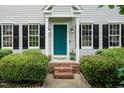 Welcoming front entrance with a blue door, brick steps, manicured bushes, and decorative wall lanterns at 3110 Trinness Dr, Durham, NC 27707