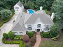 Expansive aerial view of a white brick home with a backyard pool and a detached garage among lush trees at 5005 Lenoraway Dr, Raleigh, NC 27613