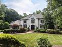 Beautiful white brick house surrounded by mature trees and lush green lawn showcasing the home's curb appeal at 5005 Lenoraway Dr, Raleigh, NC 27613