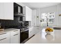 Modern kitchen with stainless steel appliances, white cabinets, black tiled backsplash, and a quartz countertop island at 1410 Joe Louis Ave, Raleigh, NC 27610