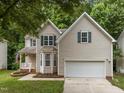 Home showcasing a two-car garage, inviting front porch, and lush landscaping at 412 Hay River St, Garner, NC 27529