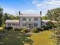 Stunning two-story white home boasting a metal roof, black shutters, and a charming balcony overlooking the meticulously maintained lawn at 301 W Thorndale Dr, Oxford, NC 27565