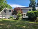 View of the rear exterior featuring an attached garage, leafy trees, and a well-maintained lawn at 5760 Hesters Store Rd, Hurdle Mills, NC 27541